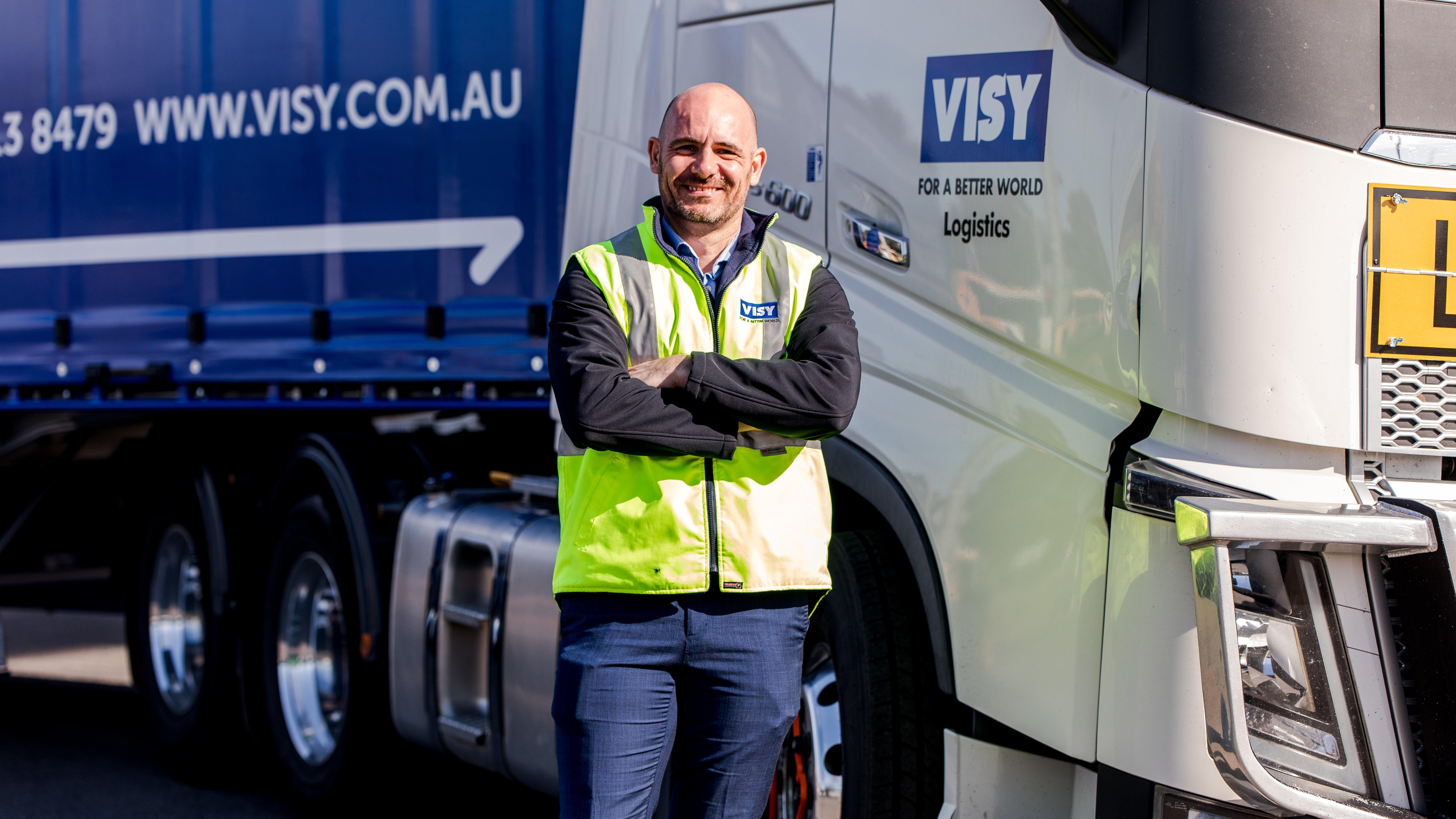 A man in a high visibility safety vest smiles at a camera in front of a Visy truck